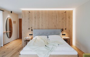 Un dormitorio moderno con cabecera de madera, un espejo grande, mesitas de noche y una cama con edredón blanco.