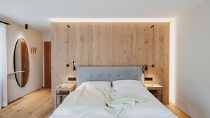 A modern bedroom with a wooden headboard, a large mirror, bedside tables, and a bed with a white comforter.