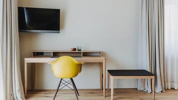 A room with a wooden desk, a yellow chair, a black bench, and a mounted TV.