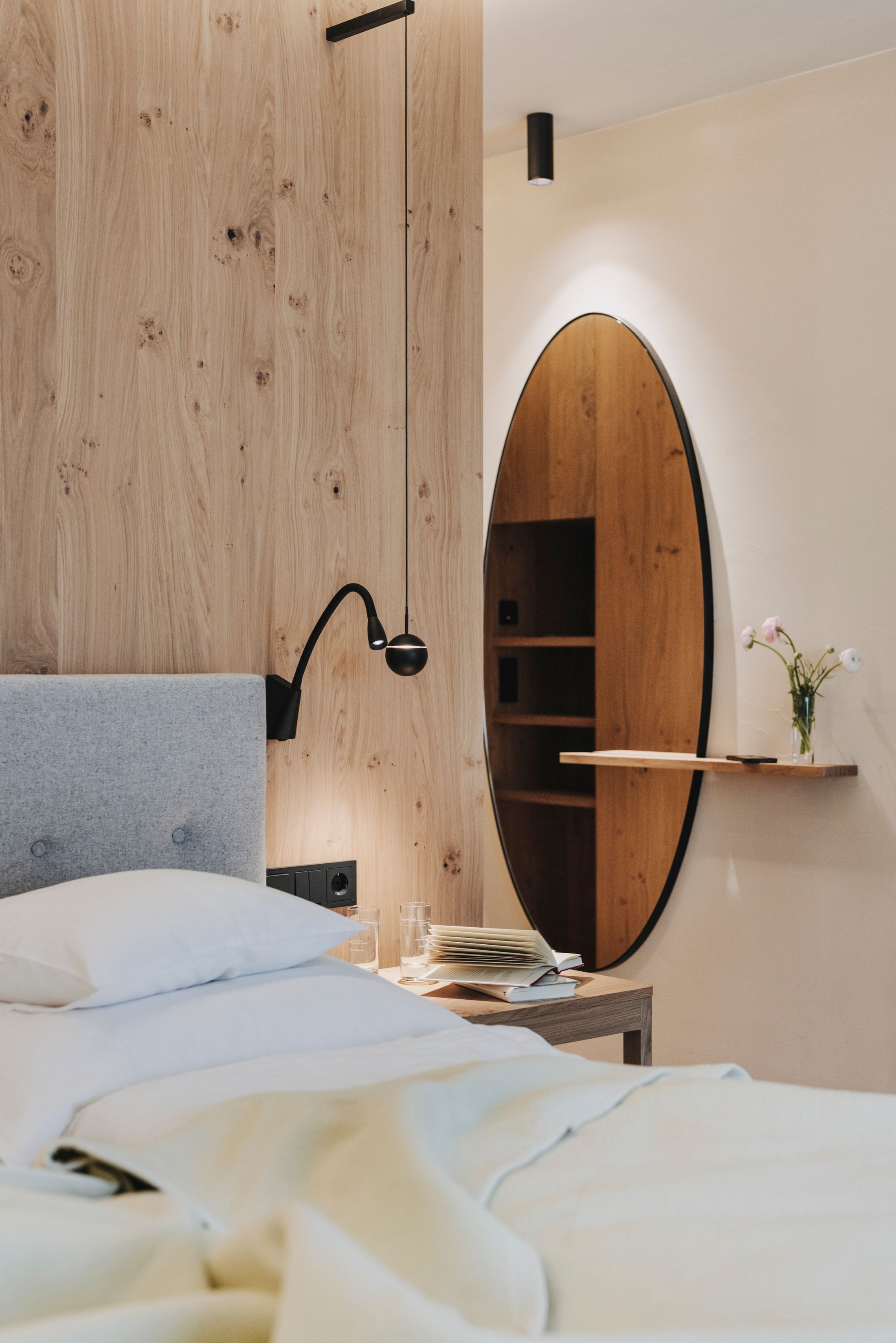 A bedroom with a bed, a bedside table, a mirror, and a wooden wardrobe.