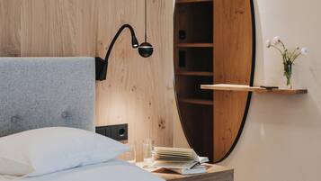 A bedroom with a bed, a bedside table, a mirror, and a wooden wardrobe.