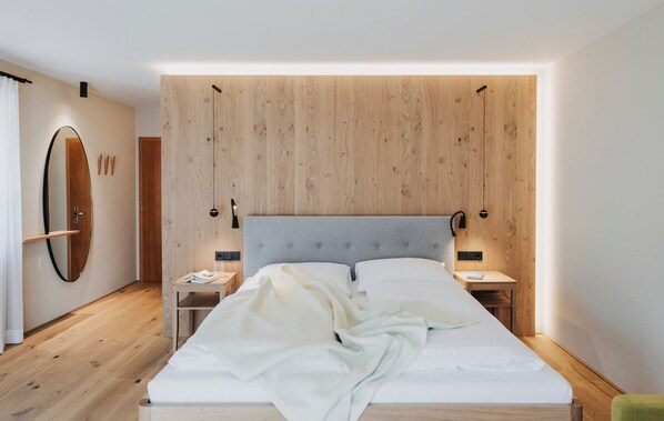 Un dormitorio moderno con cabecera de madera, un espejo grande, mesitas de noche y una cama con edredón blanco.