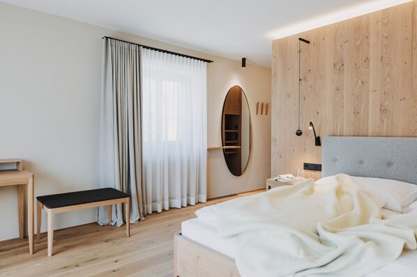 Un dormitorio con cama, mesita de noche, banco, espejo y ventana con cortinas.