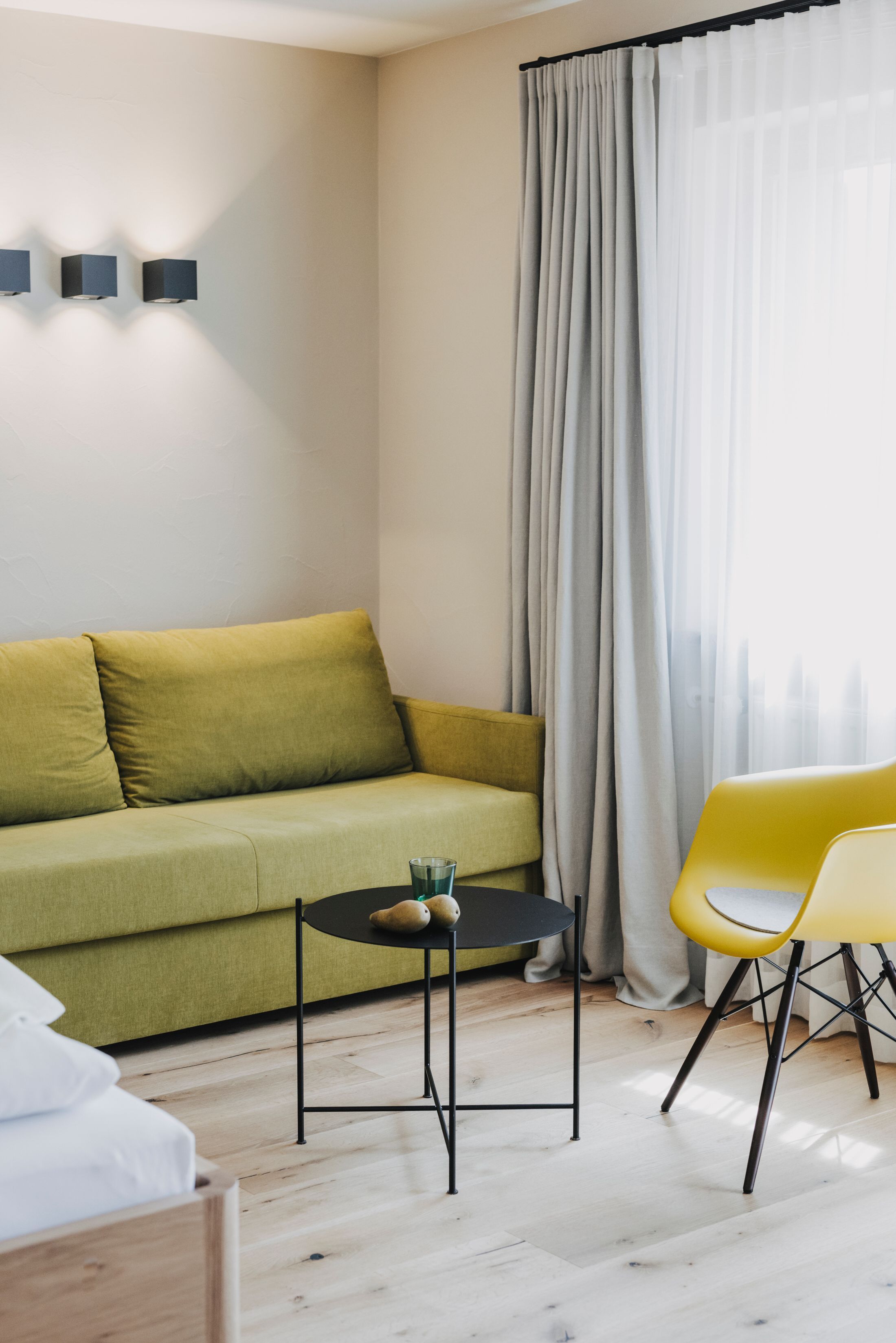 A modern living room with a green sofa, a yellow chair, a small round table with a glass, and a black lamp.