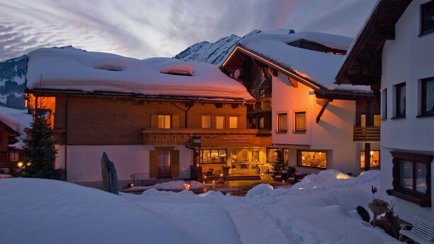 A snow-covered building with a wooden facade, a visible entrance, and a balcony overlooking a snowy landscape.
