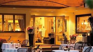 A restaurant with a wooden ceiling and a sign in German. Tables are set with wine glasses and flowers.