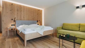 Un dormitorio moderno con una cama de cabecera de madera, un sofá verde, una mesita con dos vasos y una mesita de noche con una lámpara.