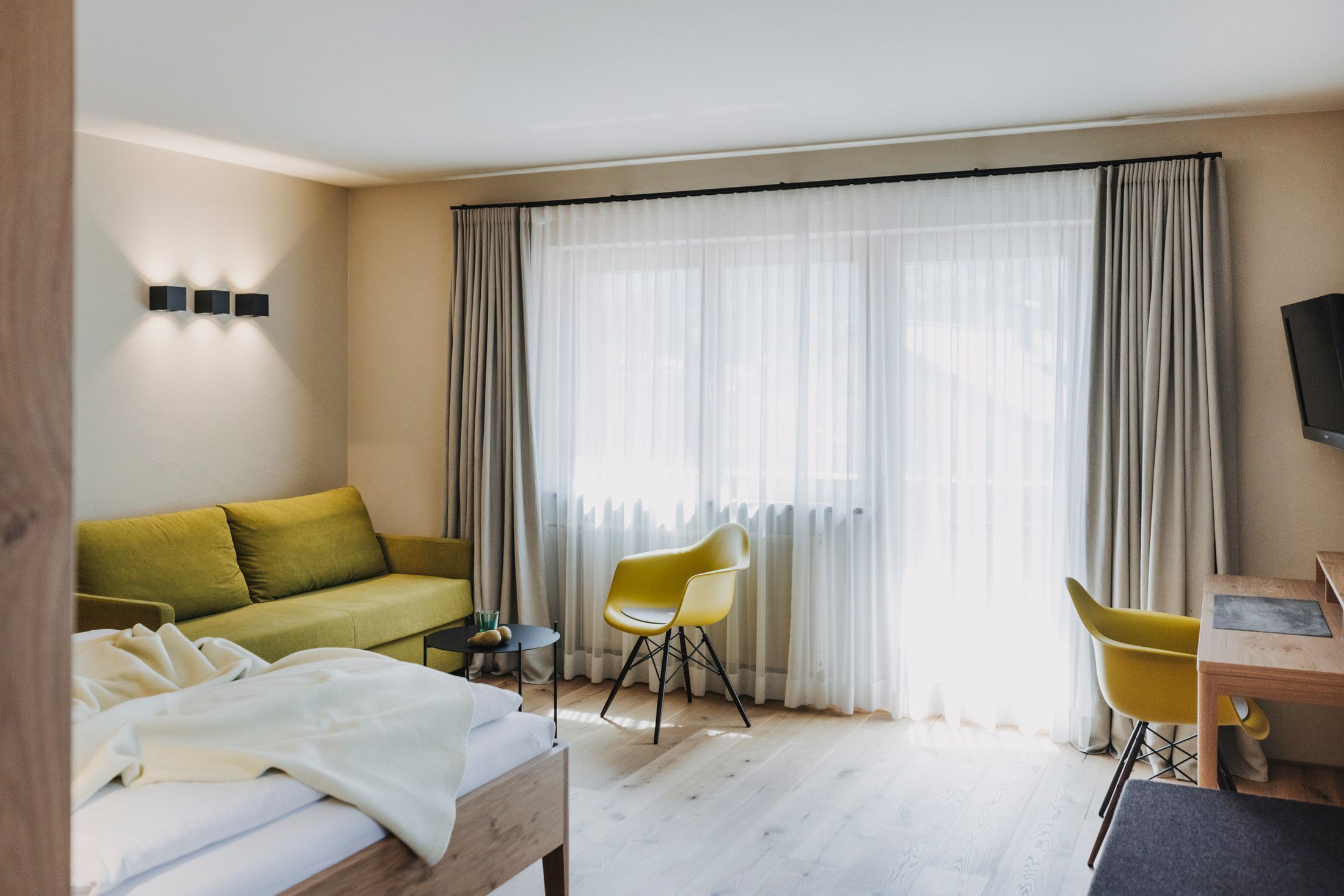 A hotel room with a bed, a sofa, two chairs, a desk, and a TV.