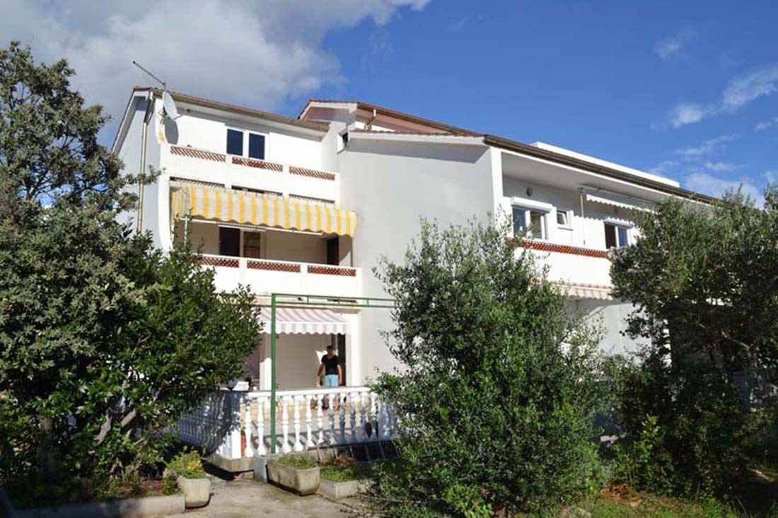 A two-story building with a balcony, a satellite dish, and a small garden area.