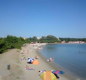 A beach with people sunbathing and swimming, and several colorful umbrellas.