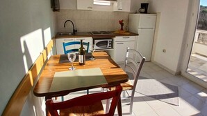 A small kitchen with a dining table and chairs, a microwave, a refrigerator, and a window with a view of the outside.