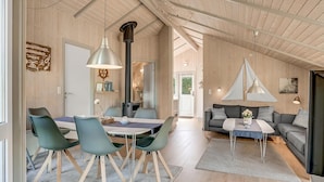 Ampla sala de estar com teto alto, paredes de madeira e área de jantar com cadeiras e mesa modernas.