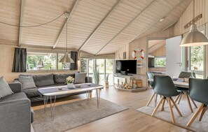 Een ruime woonkamer met een bank, salontafel en eettafel. Er is een televisie en een open haard.
