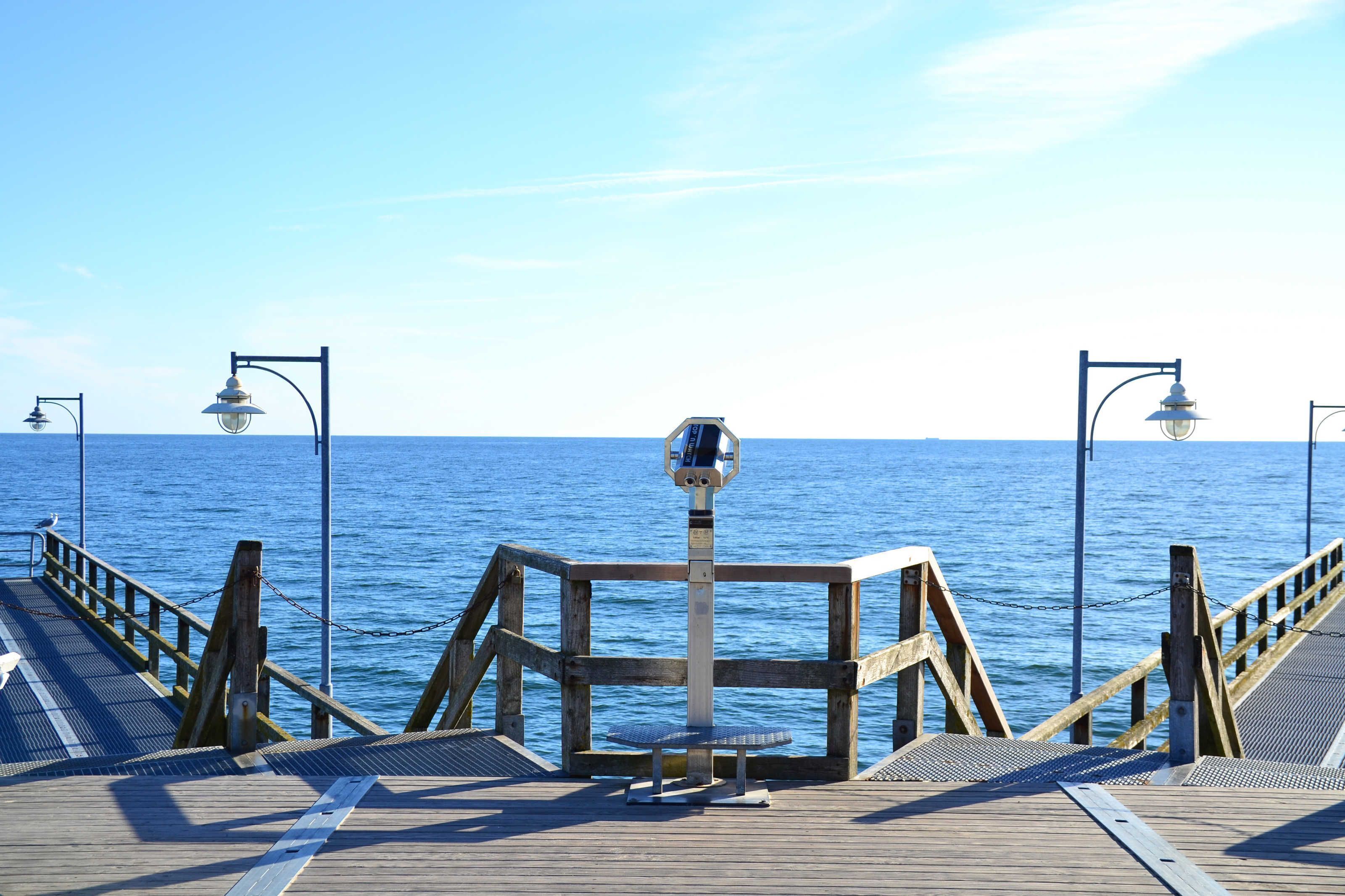 Eine Holzstege führt zu einem ruhigen Meer unter einem wolkenlosen Himmel.
