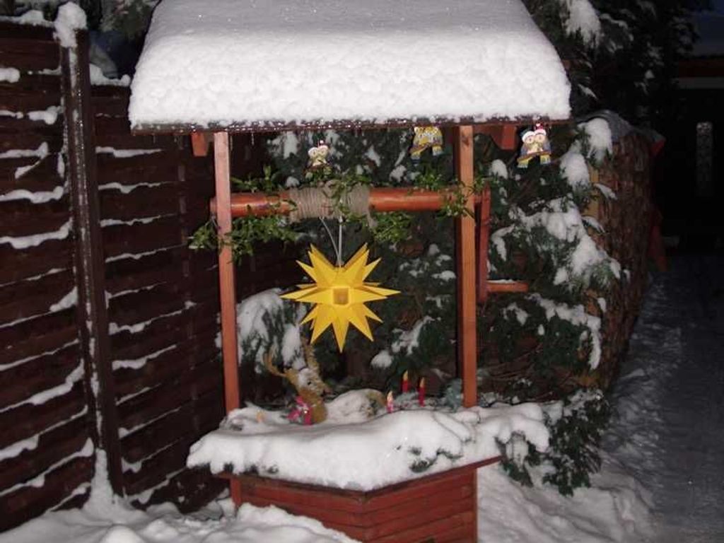 Een kerststal buiten, bedekt met sneeuw, met een ster en figuurtjes.