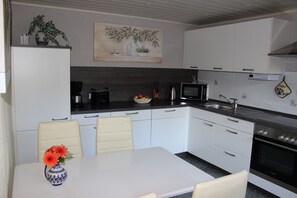 Une cuisine avec des armoires blanches, un comptoir noir, un four à micro-ondes, une cuisinière et une table à manger avec des chaises.