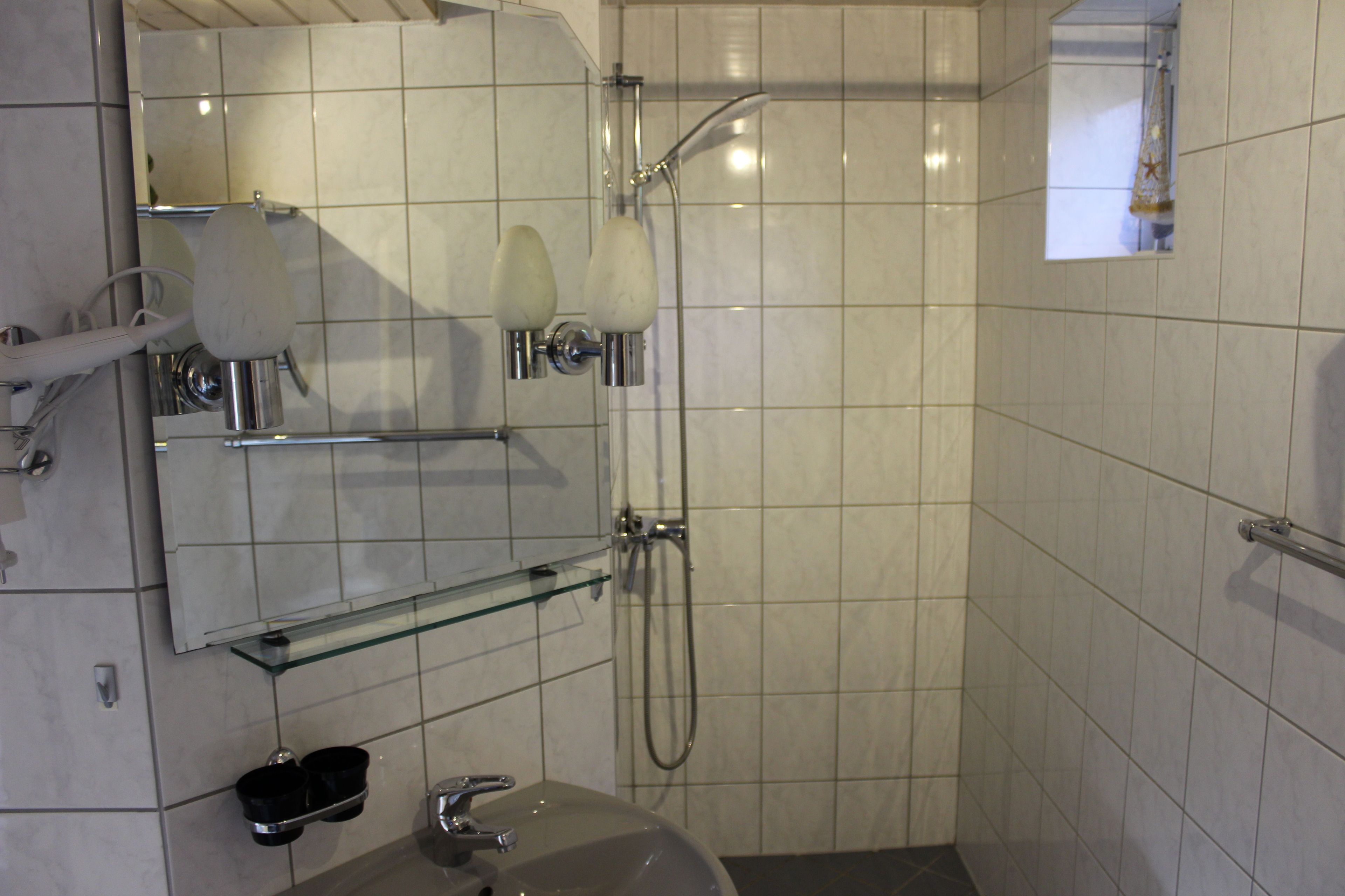 A bathroom with a glass shelf, a sink, a mirror, and a shower.