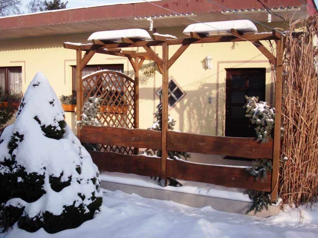 Een houten pergola met sneeuwbedekte treden en een sparrenboom bedekt met sneeuw ervoor.