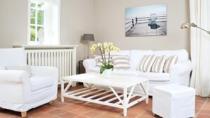 Un salon avec un ensemble de canapés blancs, une table basse blanche et un tableau accroché au mur.