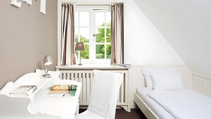 Une chambre à coucher avec un lit, un bureau et une chaise. Il y a une fenêtre avec des rideaux, un radiateur et une lampe.