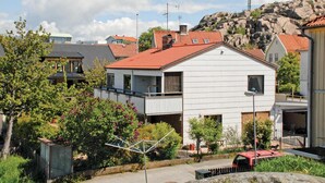Um edifício residencial de dois andares com telhado de telhas vermelhas, varanda e um pequeno jardim.