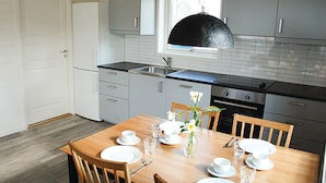 A modern kitchen with grey cabinets, a black pendant light, and a wooden dining table set with white plates, cups, and a vase with flowers.