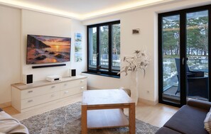 Ein modernes Wohnzimmer mit großem Fernseher, einem Holztisch, einer Couch und Blick auf eine verschneite Landschaft durch große Fenster.