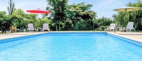 Una piscina con agua azul cristalina, rodeada de sillas de descanso y sombrillas blancas.