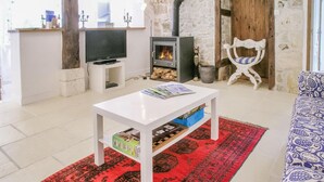 Una sala de estar con una mesa de centro blanca, un tapete rojo estampado, un sofá, un televisor, una chimenea y una pared de piedra.