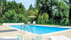 Una piscina con solárium de baldosas, sillas de descanso y una mesa con vasos.