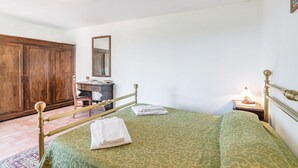 A bedroom with a bed, a wooden wardrobe, a desk with a mirror, a lamp, and a patterned bedspread. - Nice apartment in Loro Ciuffenna AR (Loro Ciuffenna AR)