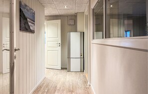 Um corredor com geladeira, porta e janela.