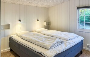 Quarto com cama, duas luminárias fixadas na parede, uma janela e uma estante embutida.