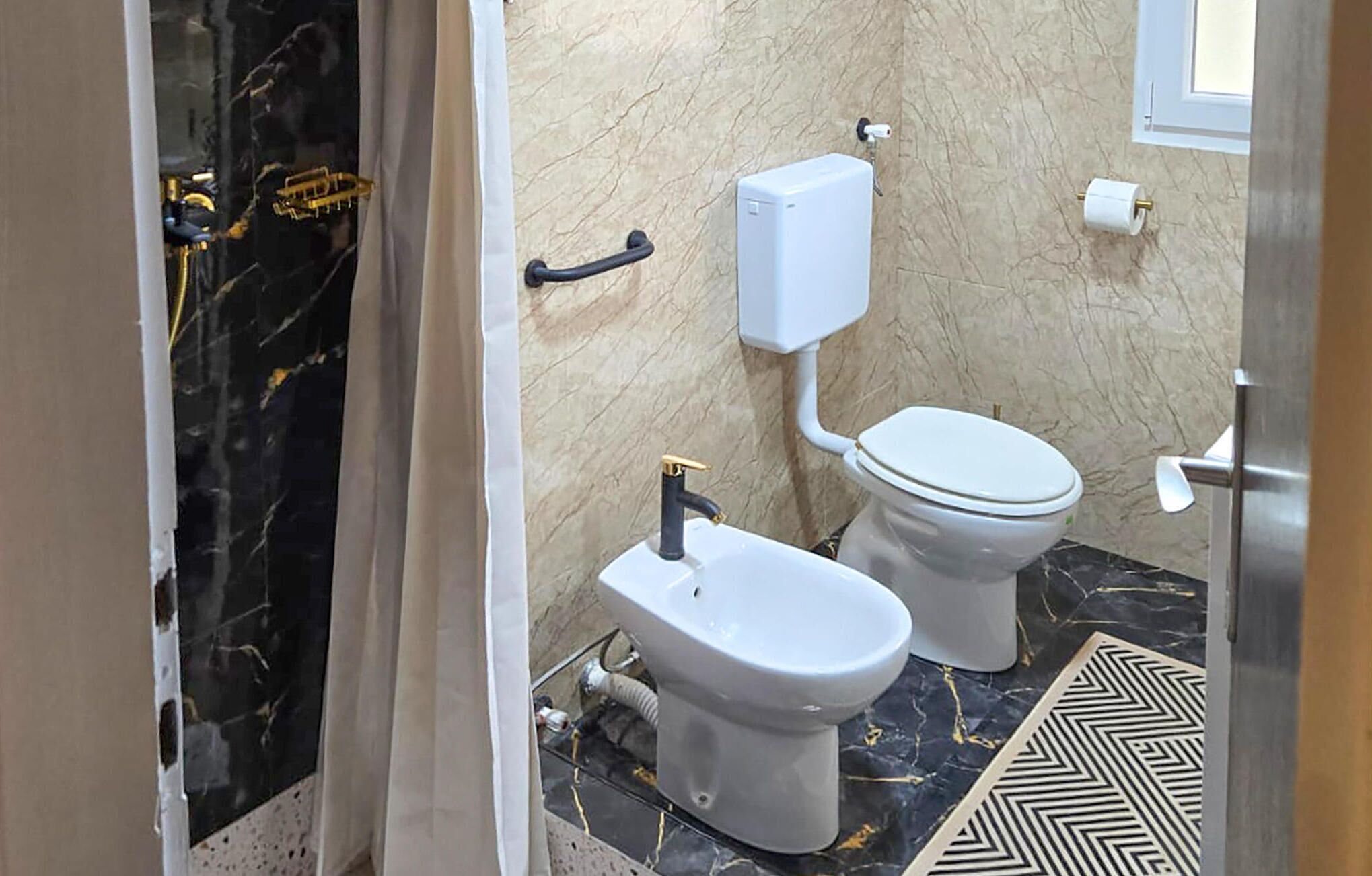 A bathroom with a toilet, bidet, marble floor, and a towel rack.