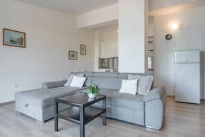 Uma sala de estar moderna com um sofá modular cinza, uma mesa de centro pequena e uma cozinha ao fundo.