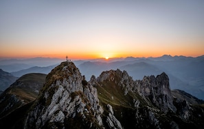 Paisaje montañoso con picos rocosos y un atardecer al fondo.
