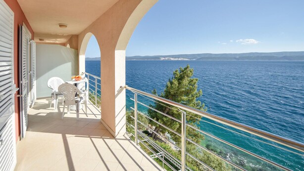 A balcony with a table and chairs, overlooking a body of water and distant land. - 1 bedroom nice apartment in Stanici (Stanici)