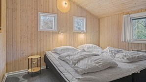 Quarto com painéis de madeira, uma cama, duas janelas e uma pequena mesa.