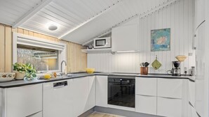 Uma cozinha moderna com armários brancos, forno preto e janela com vista para árvores.