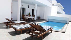 A rooftop pool area with wooden lounge chairs and a dining set.