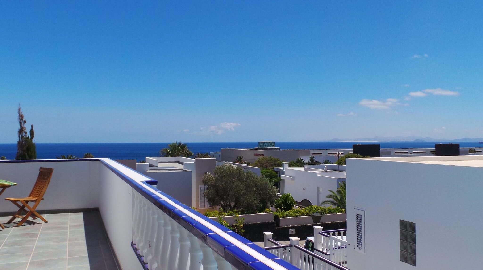 Terraço no telhado com vista para o mar, uma cadeira de madeira e edifícios brancos.