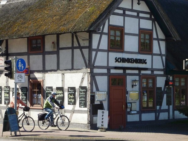 Un bâtiment traditionnel à colombages, avec une enseigne portant l’inscription « SCHINKENKRUG » et un vélo garé devant.