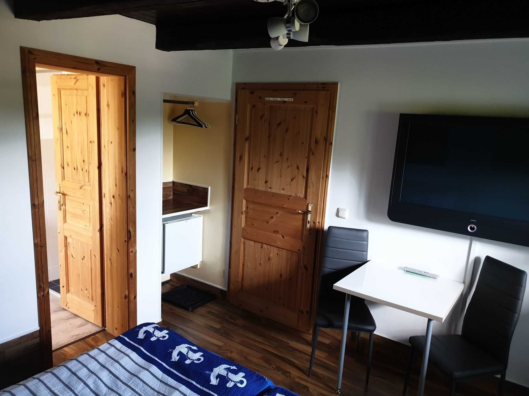 Een kamer met een bed, een bureau, een stoel, een televisie en houten deuren.