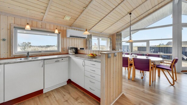 Una cocina moderna con vigas de madera, un ventanal grande y una zona de comedor con sillas moradas.