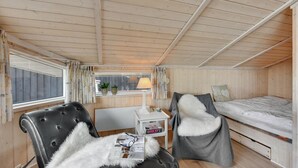 Una habitación acogedora tipo cabaña con una cama, una silla, una mesita y un ventanal con cortinas.