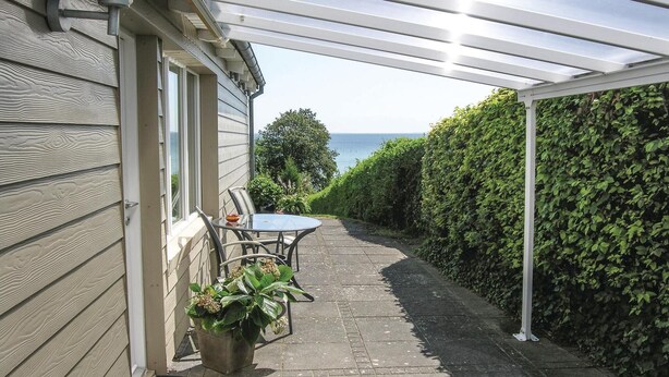 A covered patio with a table and chairs, a potted plant, and a view of the sea. - Awesome home in Rudkøbing (Rudkøbing)