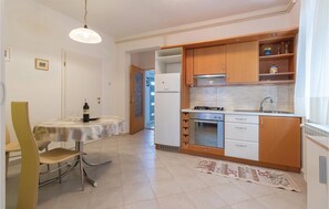 A compact kitchen with wooden cabinets, a white refrigerator, a stove, and a dining area with a table and chairs. - 1 bedroom beautiful apartment in Zadar (Zadar)