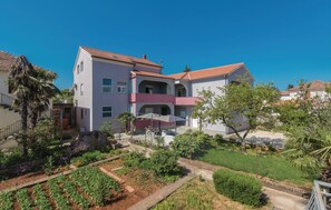 A multi-story building with a red-tiled roof, a balcony, and a garden area with various plants and a pathway. - 1 bedroom beautiful apartment in Zadar (Zadar)