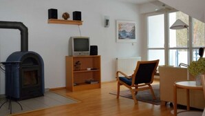 Una sala de estar con chimenea, un televisor en un estante, una silla y una mesa.