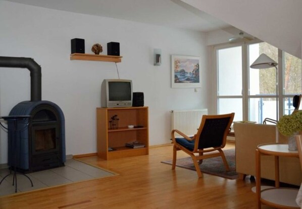 Una sala de estar con chimenea, un televisor en un estante, una silla y una mesa.